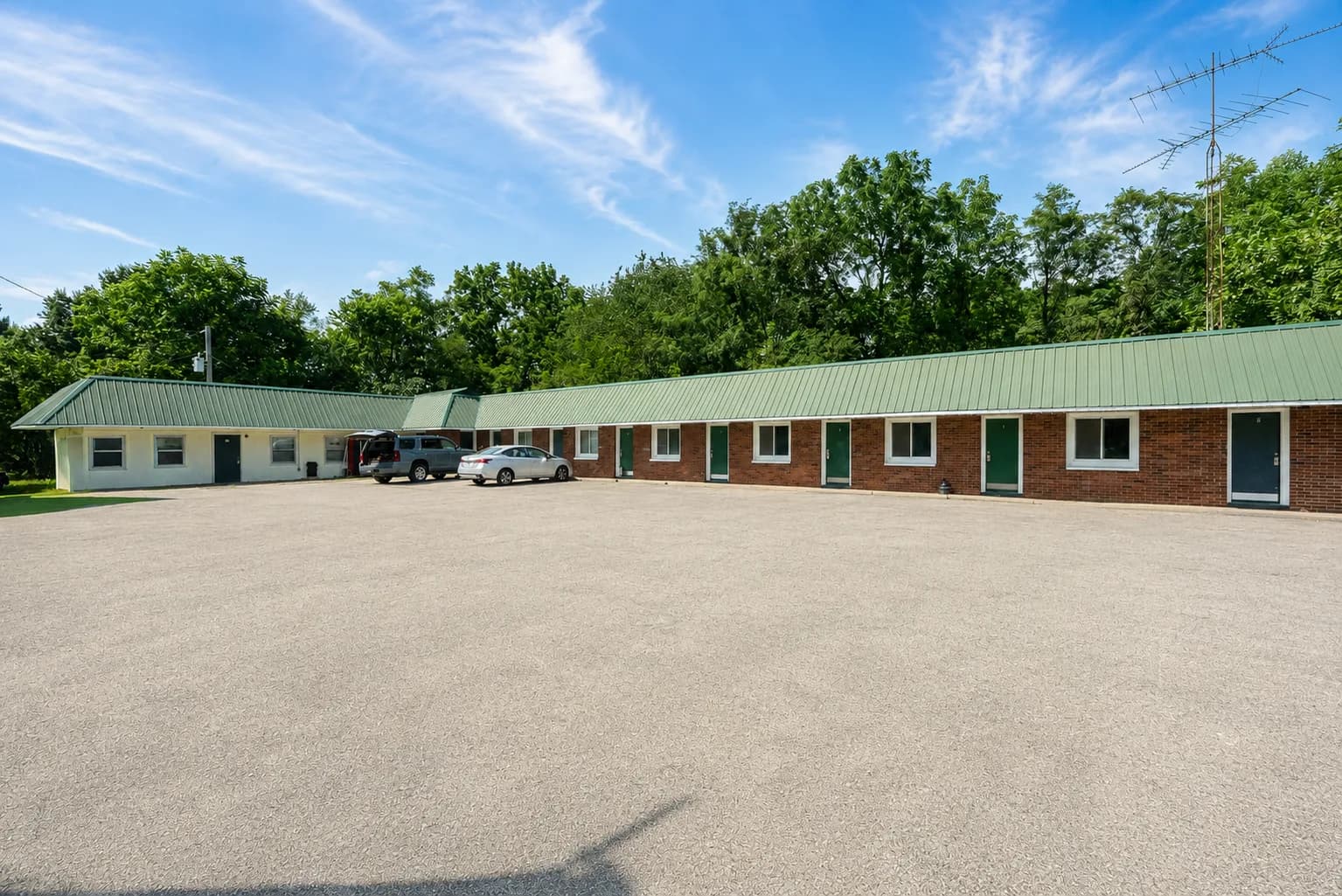 Exterior of the brick motel building with a green metal roof under a blue sky