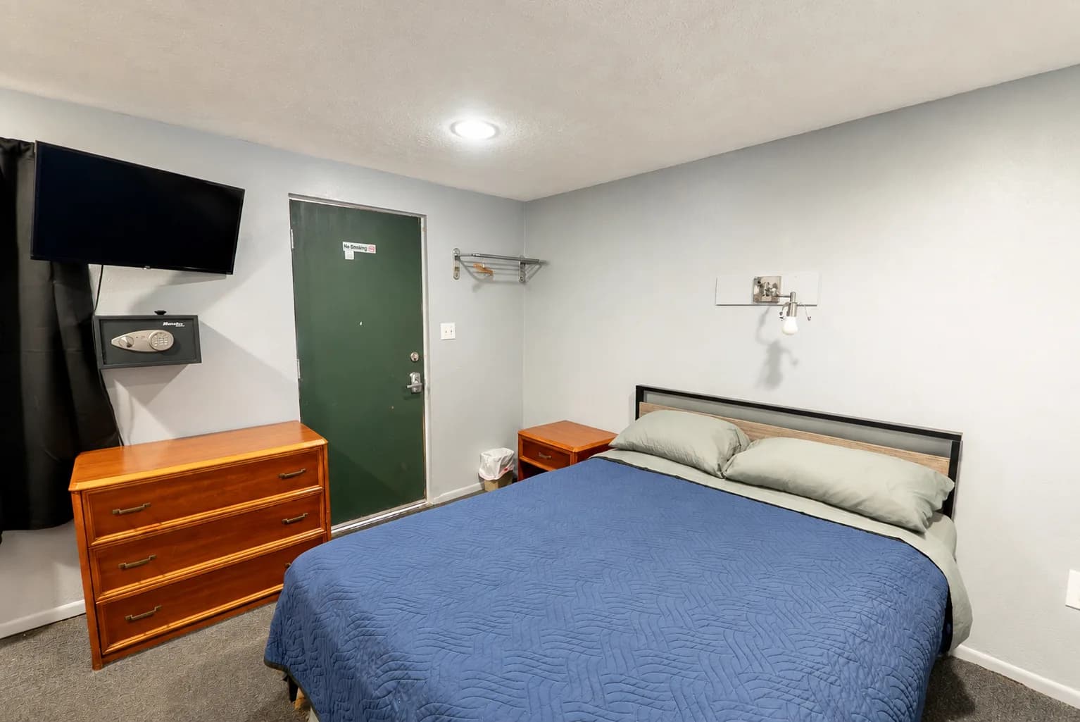 Guest room with a queen bed, wall-mounted TV, and a wooden dresser