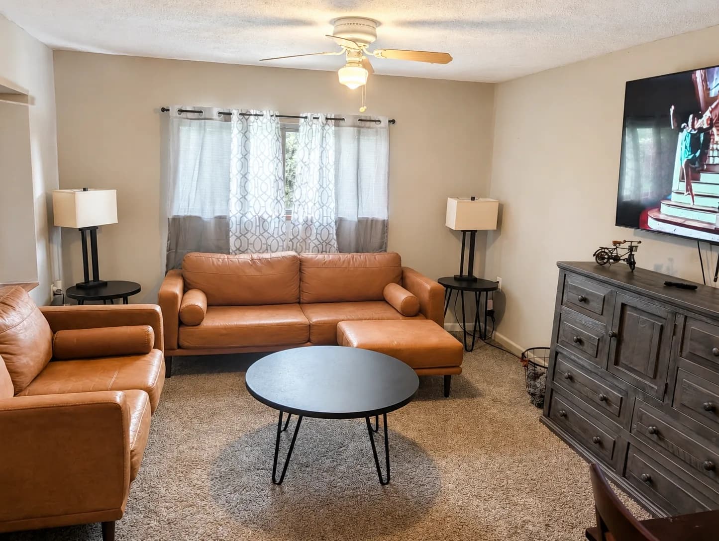 Suite living room with a leather sofa, two lamps, ceiling fan, and TV